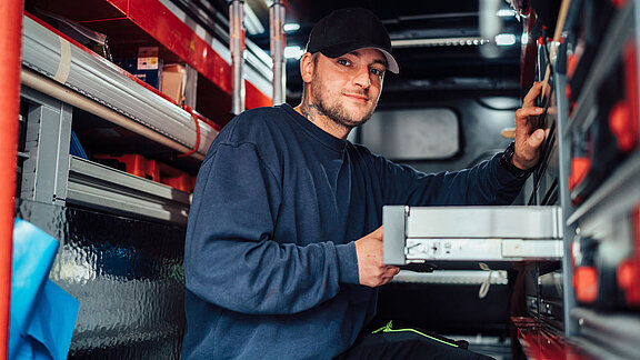 Foto eines Servicemitarbeiters im Serviceauto bei der Suche nach Materialien.