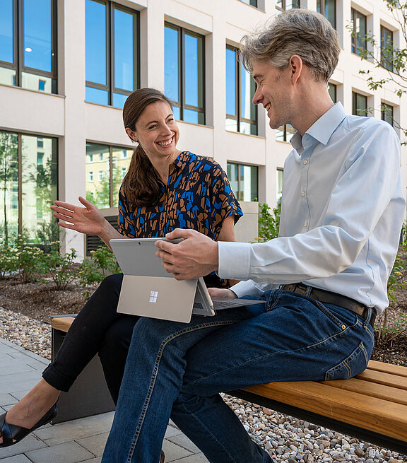 Frau und Mann sitzen auf einer Bank mit einem Tablet in der Hand 