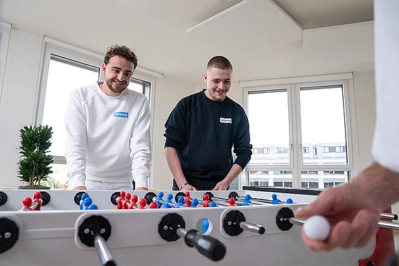 Nahaufnahme eines Tischfußball-Kickers und zwei Personen, die spielen.