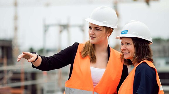 Zwei Frauen mit Bauhelm und Warnweste stehen auf dem Dach einer Baustelle