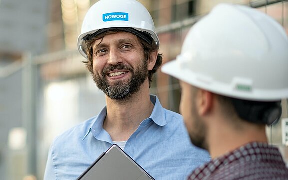 Zwei Männer mit HOWOGE Bauhelm schauen in die Ferne auf einer Baustelle