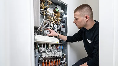 Junger Mann arbeitet an einem geöffneten Sicherungskasten an der Wand.
