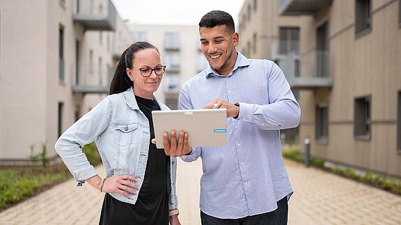 2 Mitarbeiter stehen vor einem Gebäude und schauen aufs Tablet