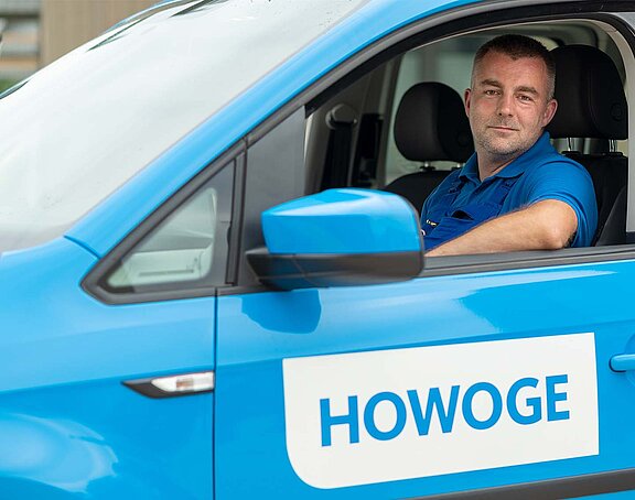 Ein Hausmeister sitzt im HOWOGE Auto und schaut aus dem Fenster in die Kamera