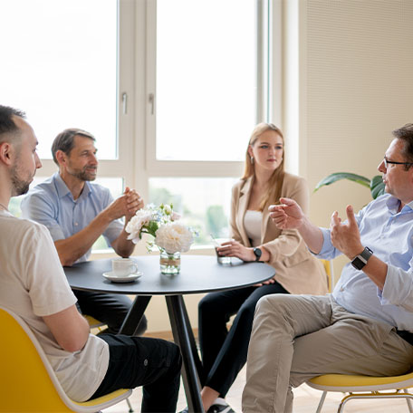 Fachkräfte und Auszubildende sitzen an einem Tisch und diskutieren miteinander