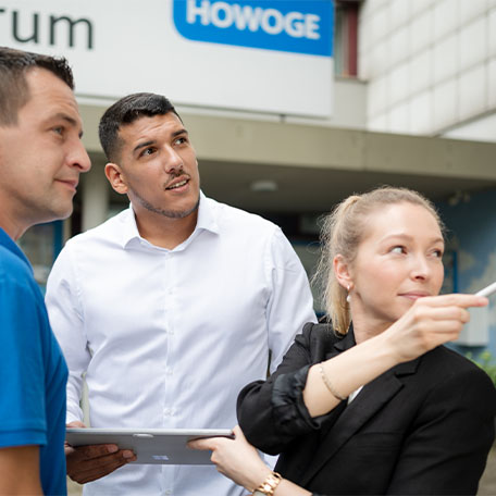 Ein Hausmeister und 2 HOWOGE Kollegen stehen vor dem Kundenzentrum.
